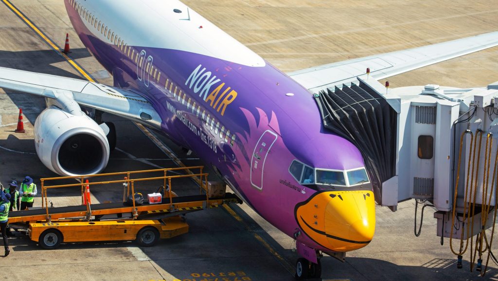 Nok Air airplane docked at an airport gate with vibrant livery and ground crew.